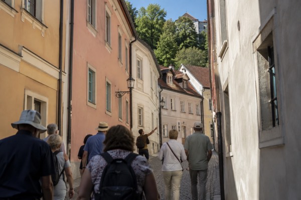 A guided group walking together up a narrow old-town lane behind their guide, pastel house fronts on both sides, Ljubljana Old Town, Ljubljana