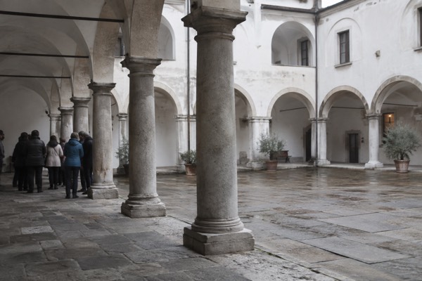 An arcaded courtyard of plain stone columns, a small group standing in the shade listening to their guide, Krizanke, Ljubljana