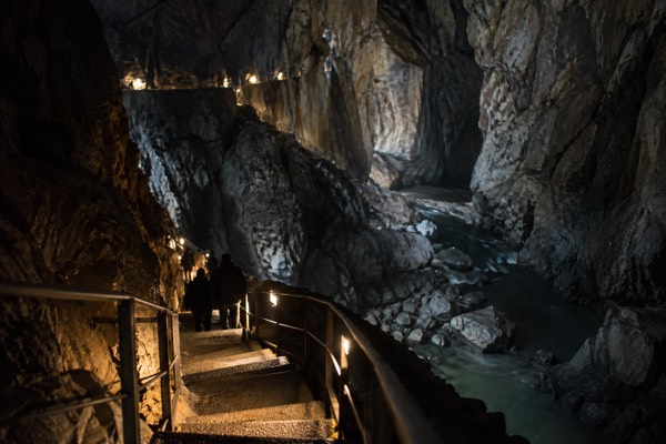 A steep flight of steps descending underground into a huge dark limestone chamber, handrails catching the lamplight, Skocjan Caves, Divaca