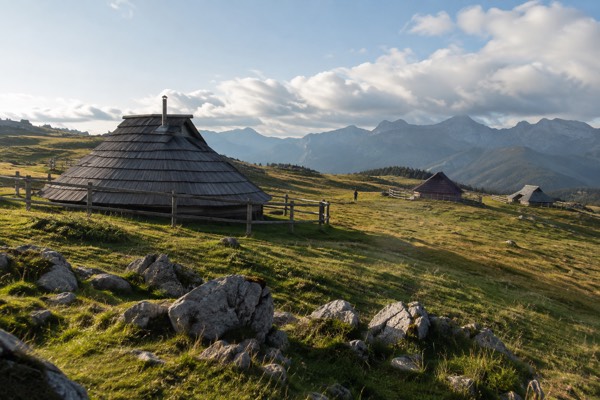 Low oval herdsmen's huts with steep shingled roofs scattered across a high open pasture under drifting cloud, Velika Planina, Kamnik