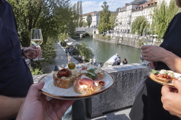 Small tasting plates and glasses handed round a standing group on a city street, the food filling the foreground, Ljubljana City Centre, Ljubljana