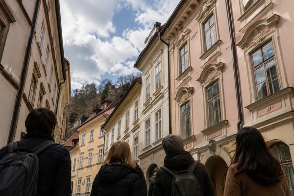 A guide with a small group in a narrow cobbled old-town lane, everyone looking up at the house fronts, Ljubljana Old Town, Ljubljana