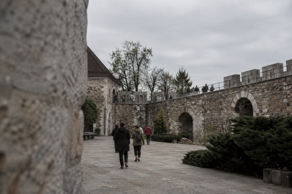 The walled courtyard of a wooded hilltop castle, visitors crossing the flagstones towards the ramparts, Ljubljana Castle, Ljubljana