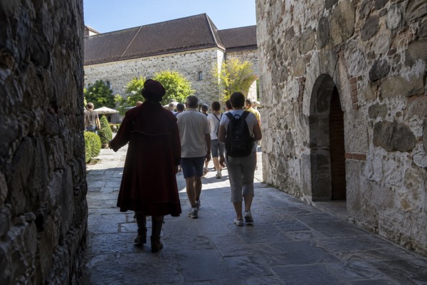 A guide in period costume leading visitors along a stone passage inside a castle wall, Ljubljana Castle, Ljubljana