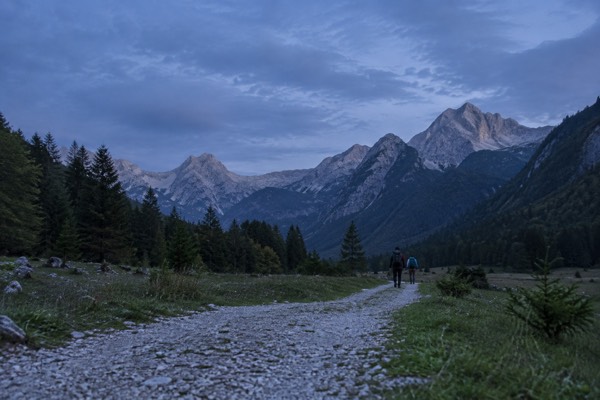 A gravel track running into a wide alpine valley of meadow and pine under bare grey peaks, Triglav National Park, Bovec