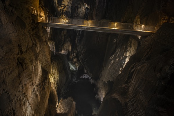 A footbridge crossing high above an enormous underground gorge, a river running far below in the dark, Skocjan Caves, Divaca