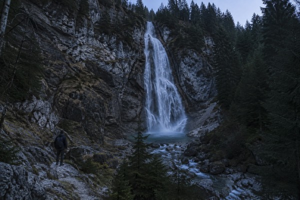 A tall waterfall dropping down a grey rock face into a pool, pines crowding the slope on either side, Kranjska Gora, Slovenia