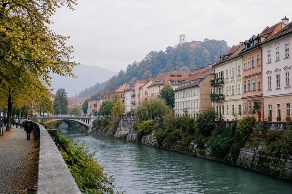 Turquoise river water flowing over smooth stones between grassy banks with mountains behind