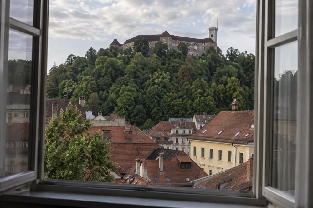 Hotel guest room window overlooking red rooftops and Ljubljana castle on its hill