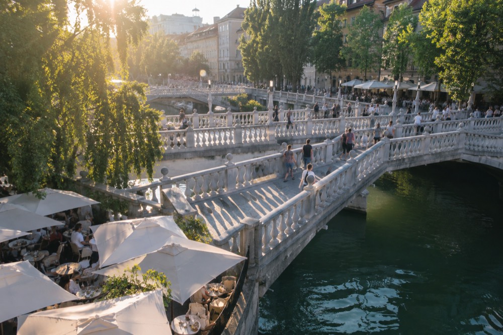 Cafe tables along the Ljubljanica river with the triple bridge in bright June sunlight