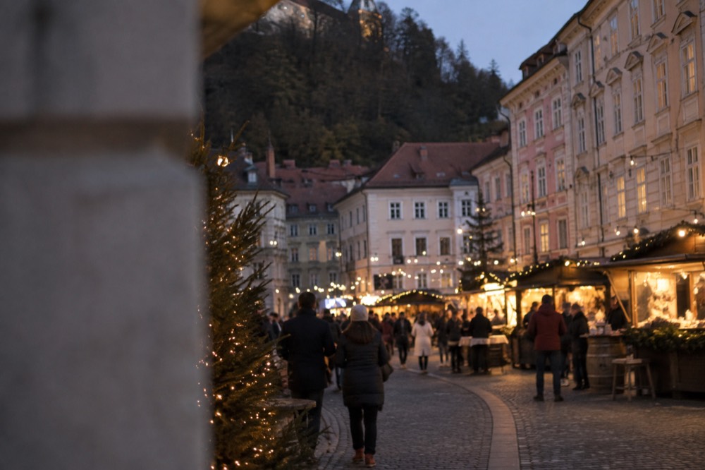 Festive market stalls and string lights along a Ljubljana square in early evening