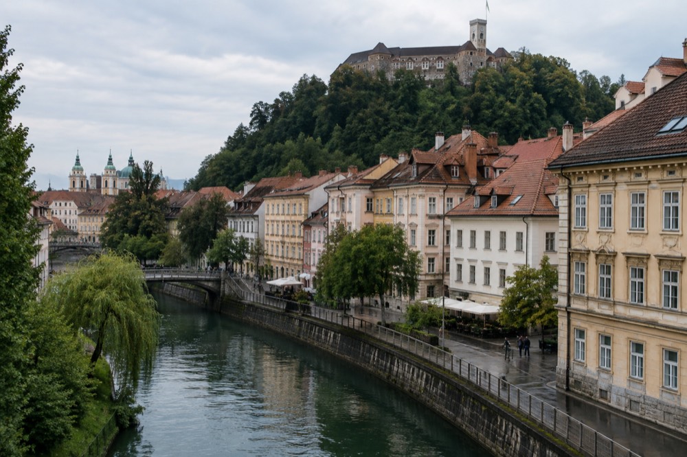 The Ljubljanica river curving past the old town buildings with the castle on the hill above