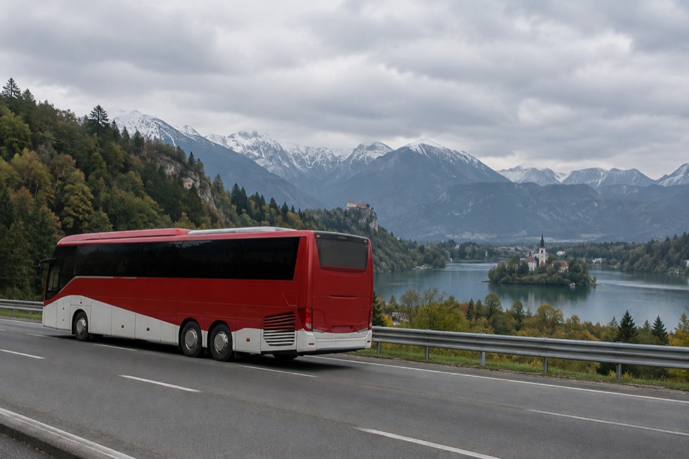 A red and white coach travelling on a motorway with forested hills in the background