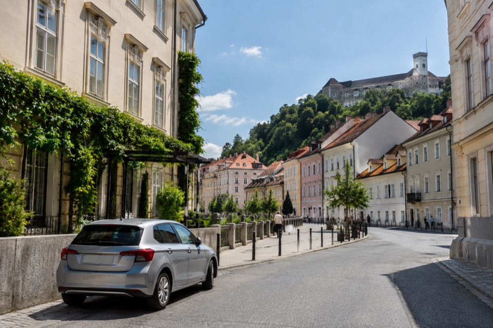 A rental car parked on a wide street with Ljubljana Castle visible on the hill above the rooftops
