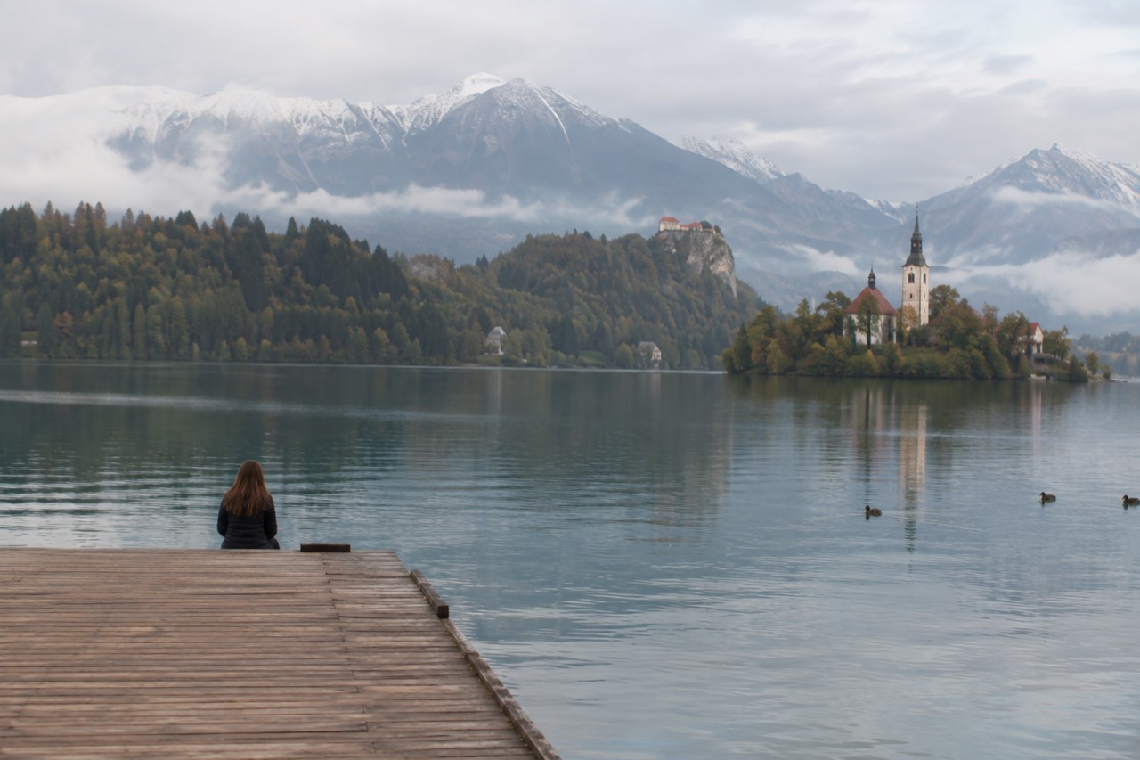 Wooden jetty on the shore of Lake Bled with forested hills behind calm water