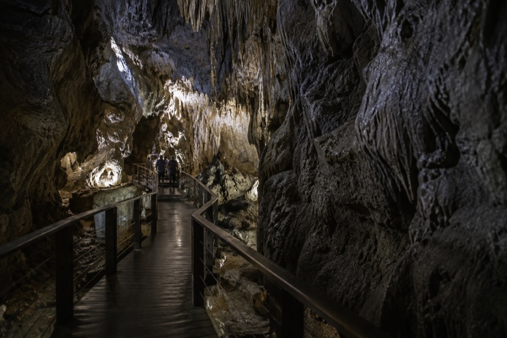 A wooden walkway winding through a large dimly lit limestone cave cavern