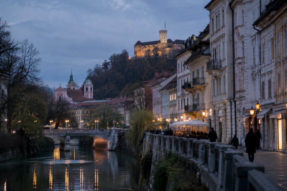 An alpine lake with a small island church and a cliff-top castle under morning light