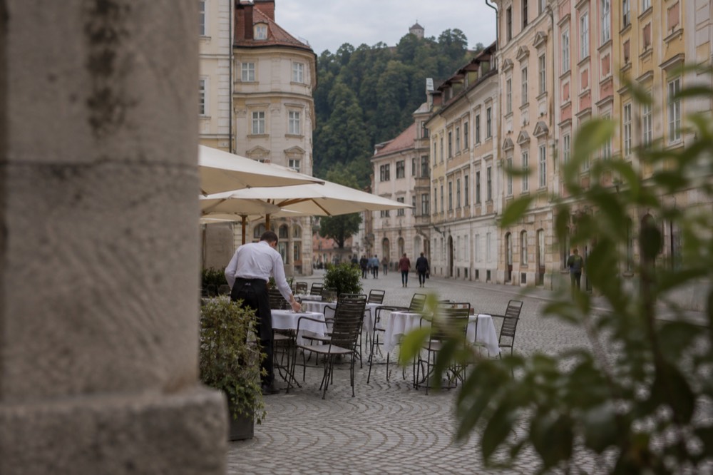 A waiter setting tables outside a café on a cobbled square in the Ljubljana Old Town