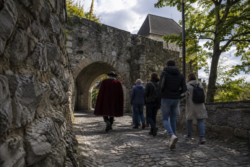 A costumed guide leading a small group through an arched stone passage inside Ljubljana Castle