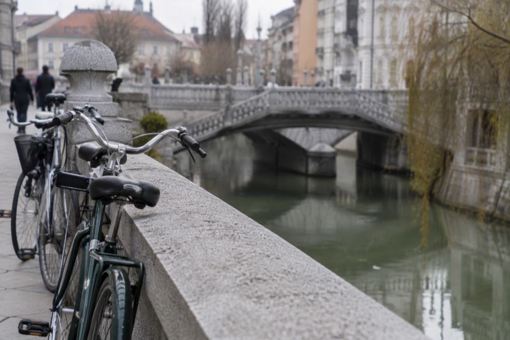 Bicycles parked beside the Ljubljanica river with the triple bridge in the background