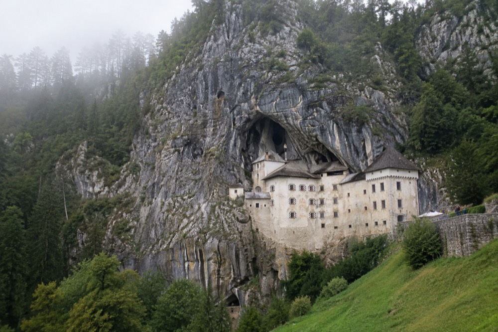 The cliff face at Predjama with the castle built into the rock above green woodland