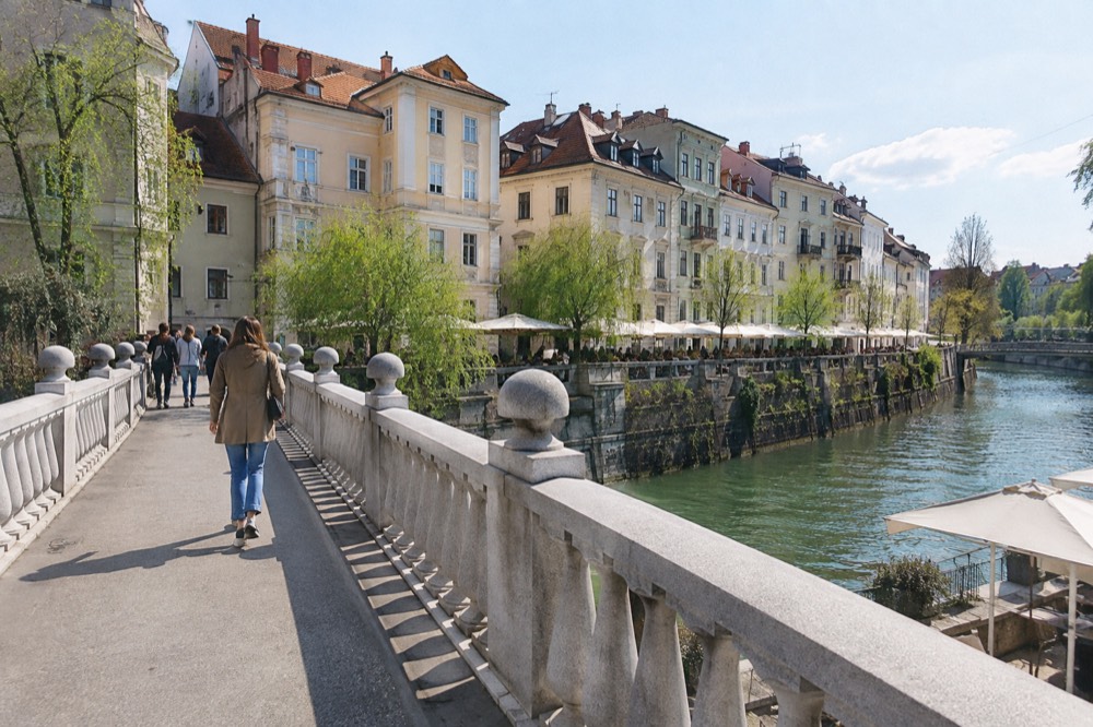 The Ljubljanica river lined with outdoor tables and pastel facades on a bright morning