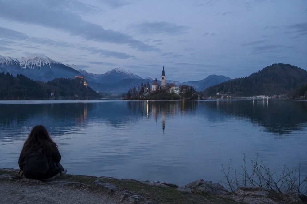 The island church on Lake Bled seen across calm water with wooded hills behind