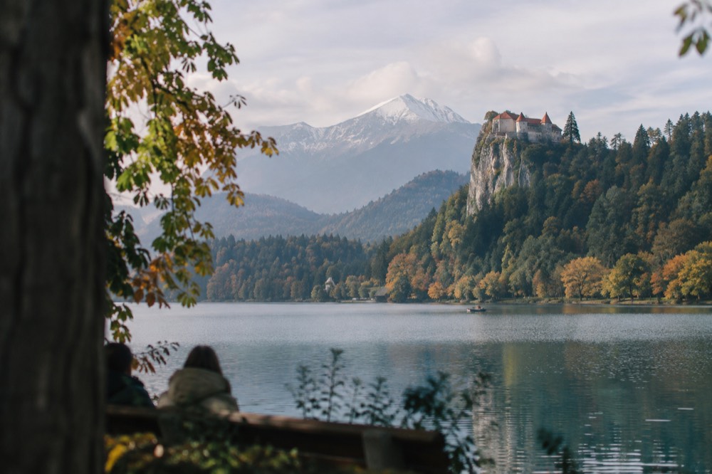 Bled Castle on its cliff above the lake with autumn colour on the shoreline trees
