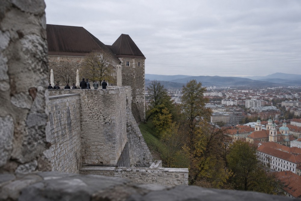 Stone ramparts of Ljubljana Castle with the city's church towers and rooftops below under an open sky