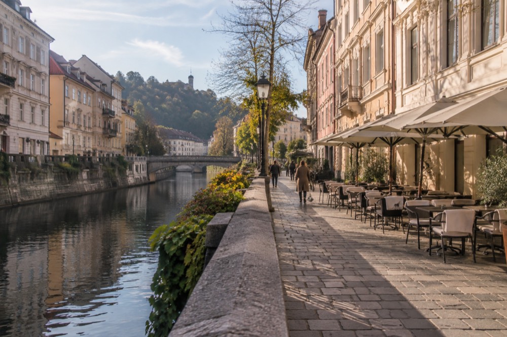 A riverside promenade in Ljubljana with outdoor tables and baroque building facades