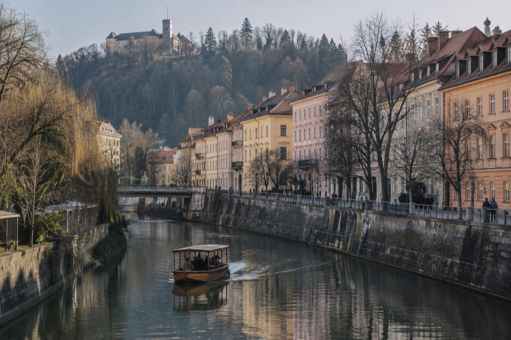 A wooden boat on a calm alpine lake with a cliff-top castle above green water