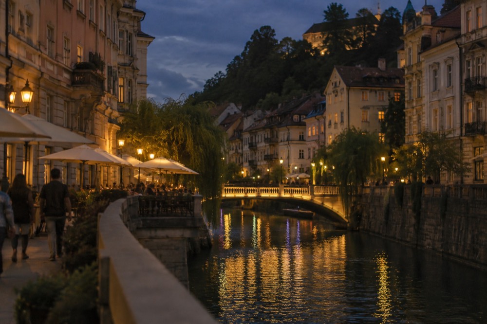 An evening riverside scene with lit bridges and restaurant terraces along the river