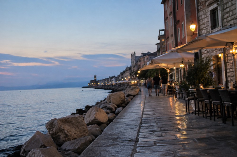 Piran: evening light on a stone seafront promenade with cafe tables and calm water