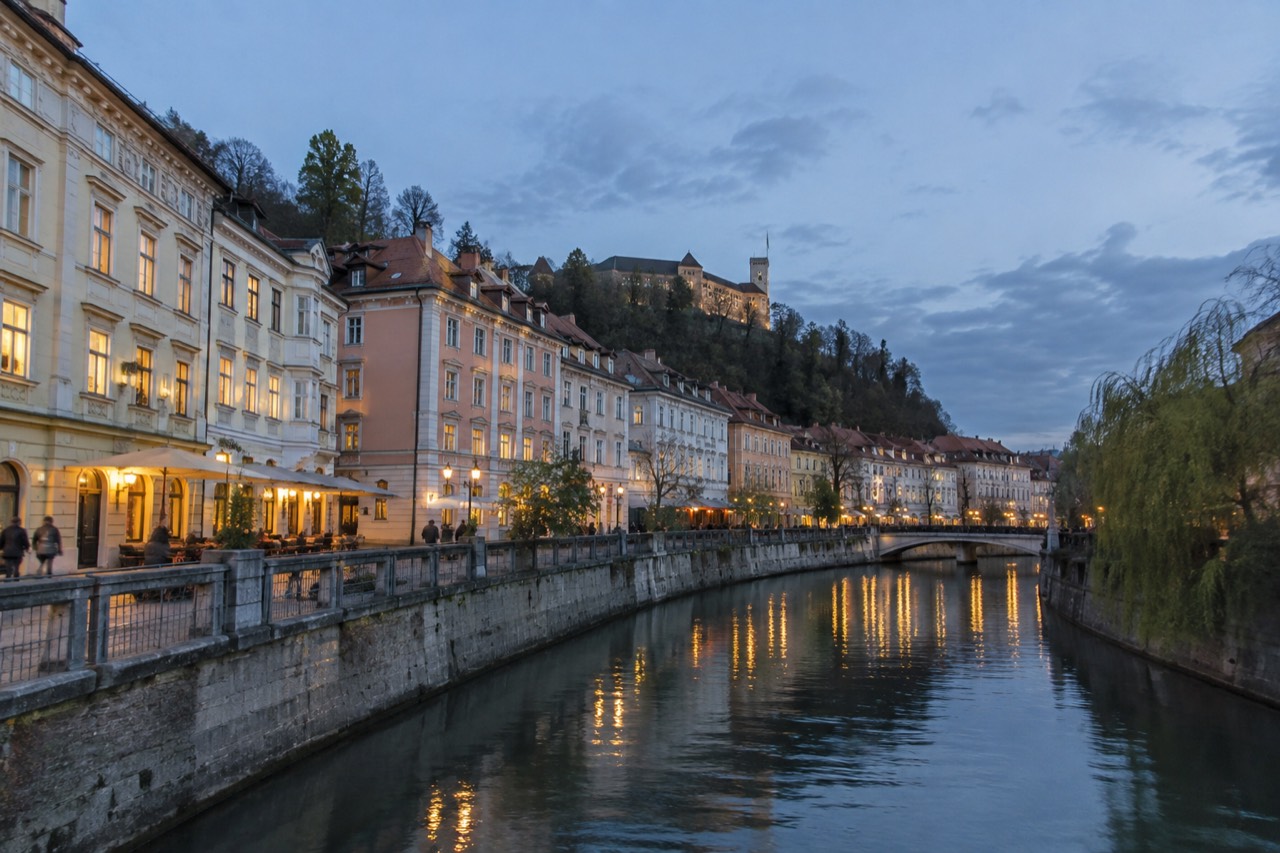 Pastel buildings beside a calm river in the centre of Ljubljana at dusk