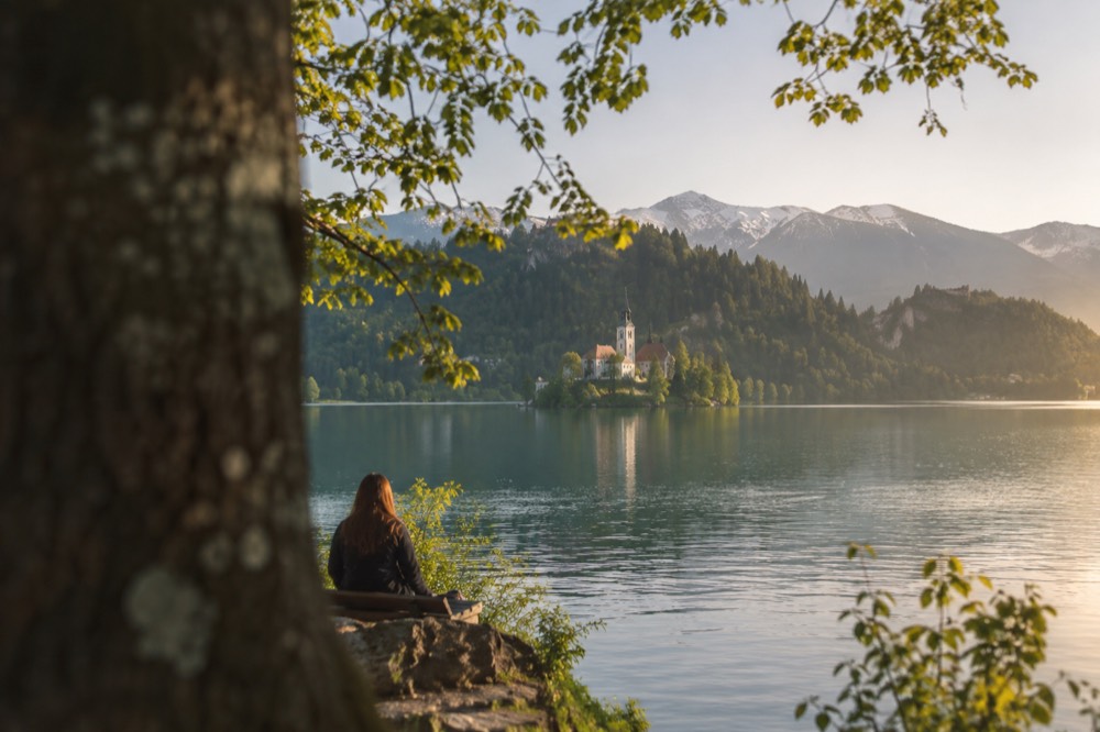 A calm Lake Bled in early morning with forested hills rising behind the water