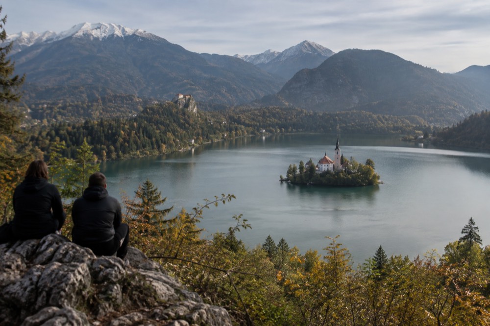 Lake Bled seen from above, with the island church in the middle of the water and forested hills around the shore