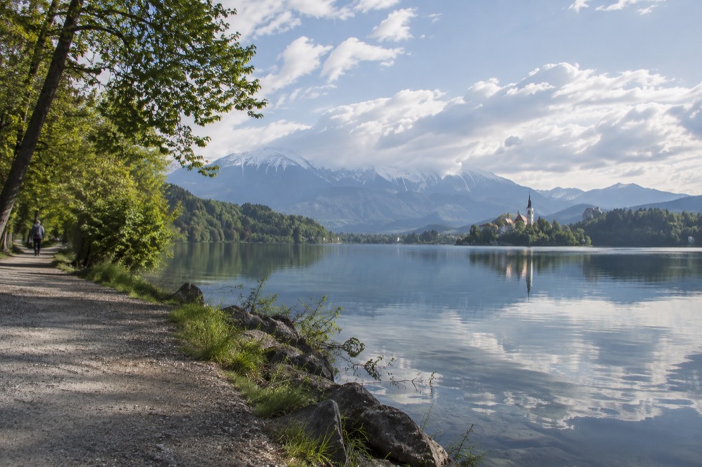 A quiet path along the shore of Lake Bled in early morning light, with calm water and trees reflected