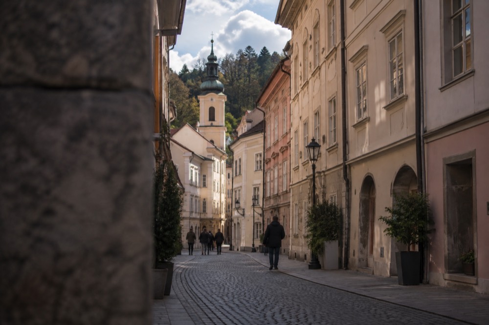 Narrow stone street with pastel facades leading towards a bell tower