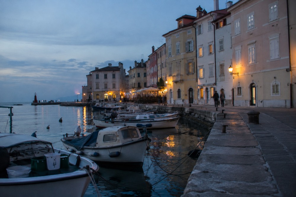 Piran harbour wall with small fishing boats moored beside pastel townhouses
