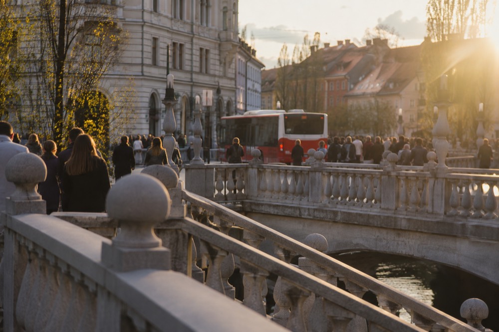 A red and white Ljubljana city bus pulling away from a stop near the Triple Bridge