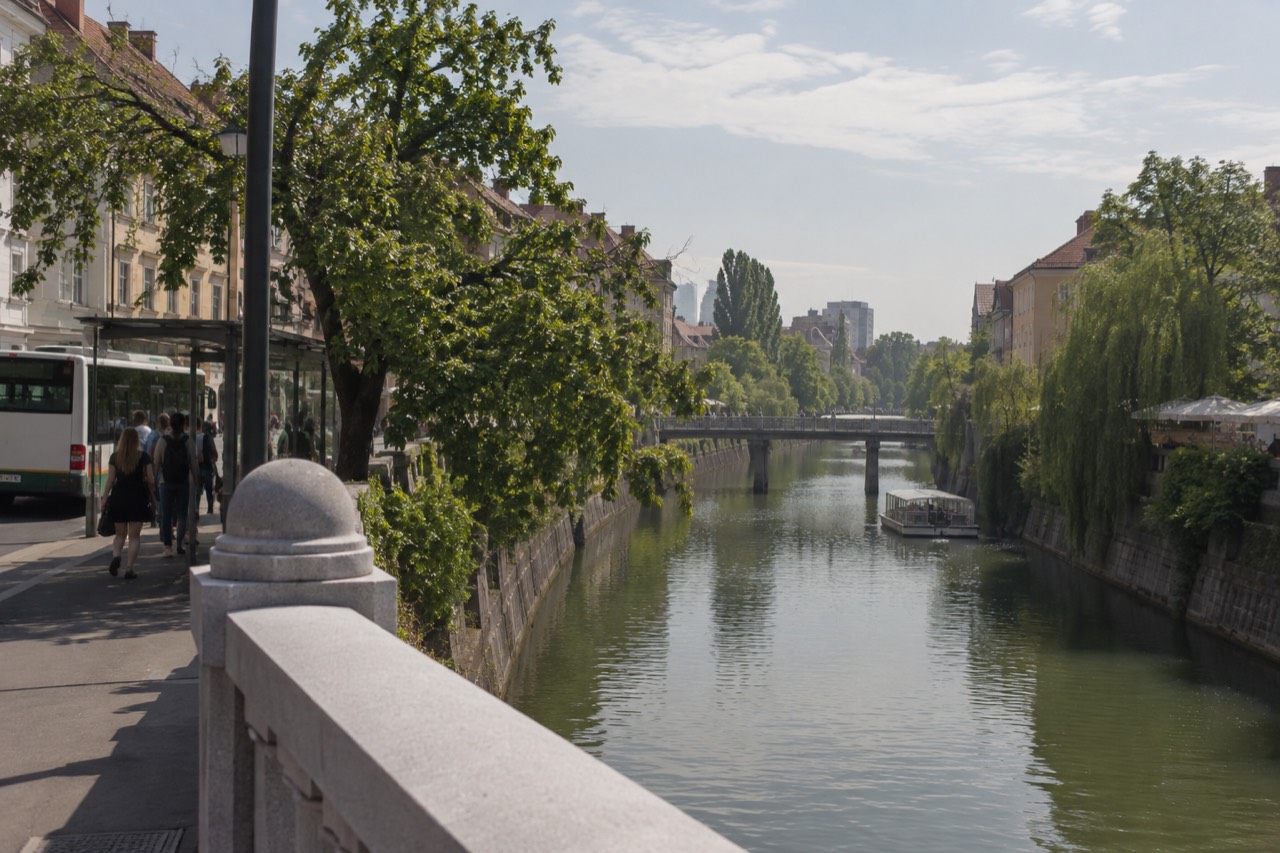 A Ljubljana city bus at a stop beside the Ljubljanica river on a bright morning