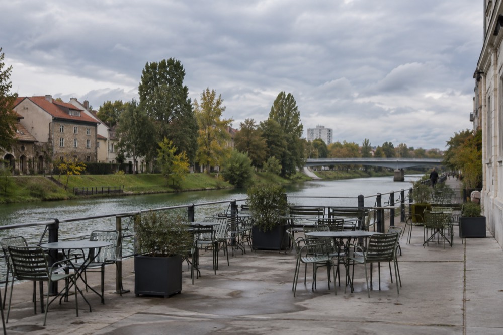 Empty riverside terrace with tables and chairs under a grey sky beside a river