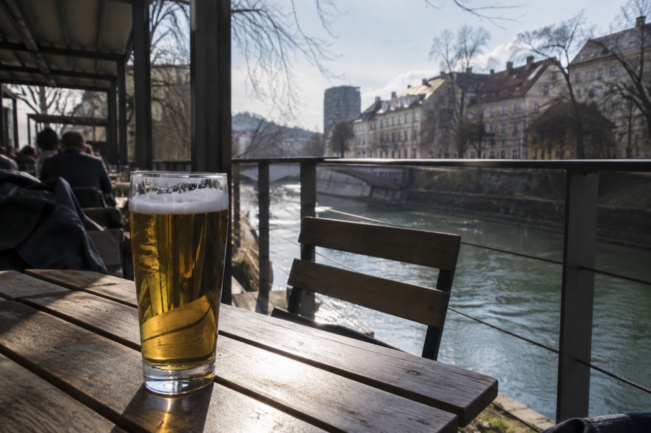 A half-litre glass of golden beer on a wooden table on a riverside terrace