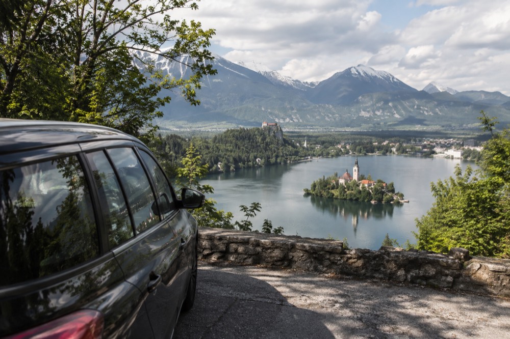 A car parked on a road above Lake Bled with the lake and island church in view below