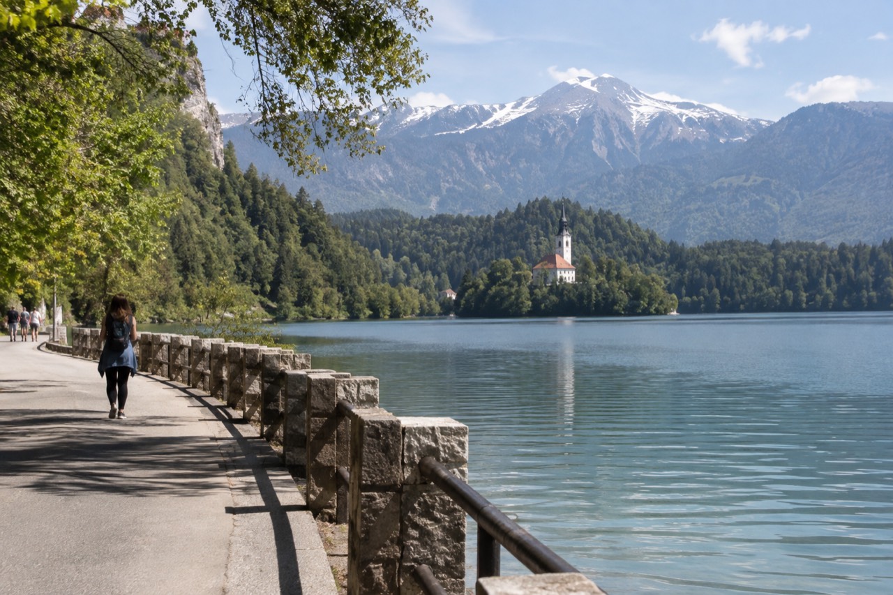 A quiet lakeside road beside Lake Bled with forested hills rising behind the water
