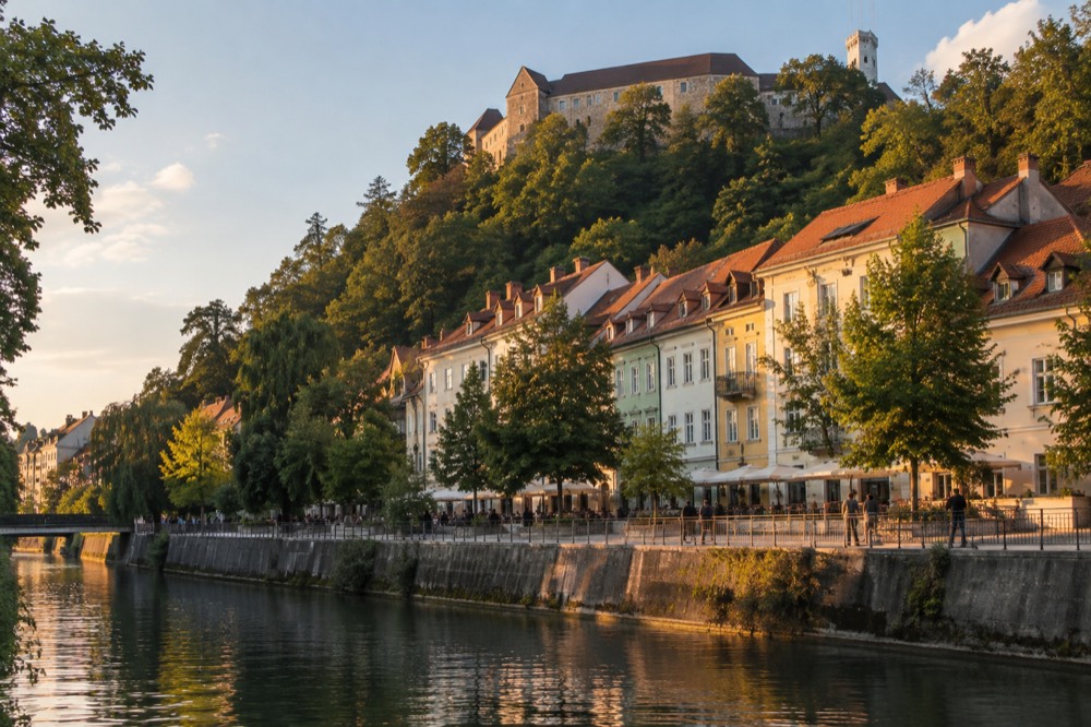 Pastel buildings along the Ljubljanica river in Ljubljana with the castle hill rising behind them