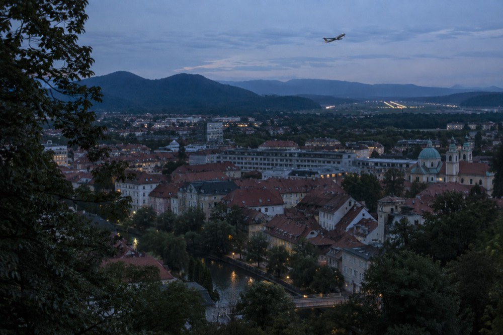 A small aircraft banking over green hills toward a regional airport runway
