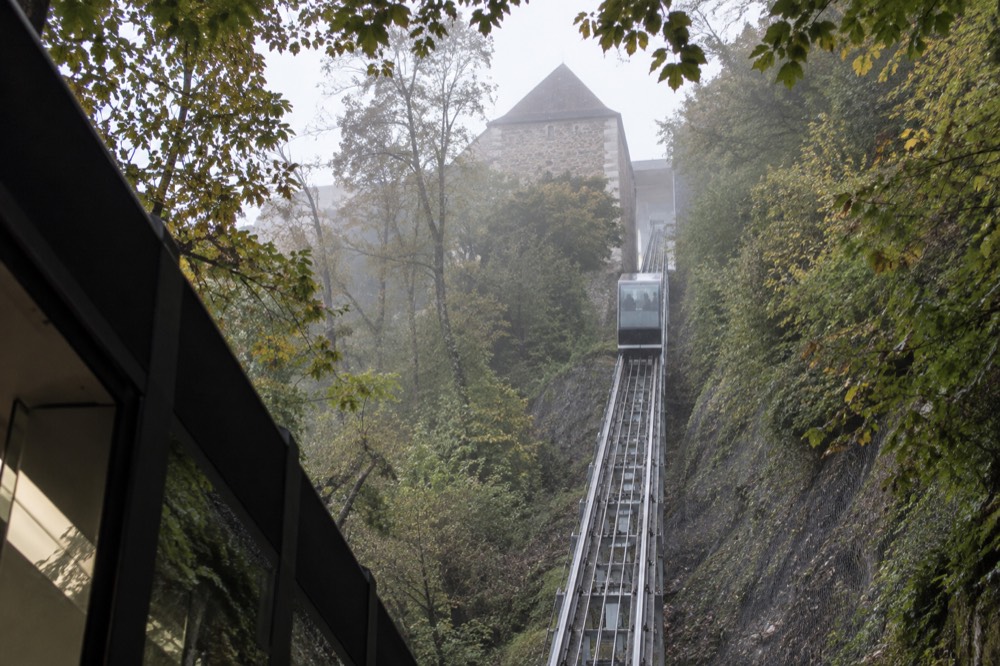 The glass funicular car climbing the cliff between the lower station and the castle walls