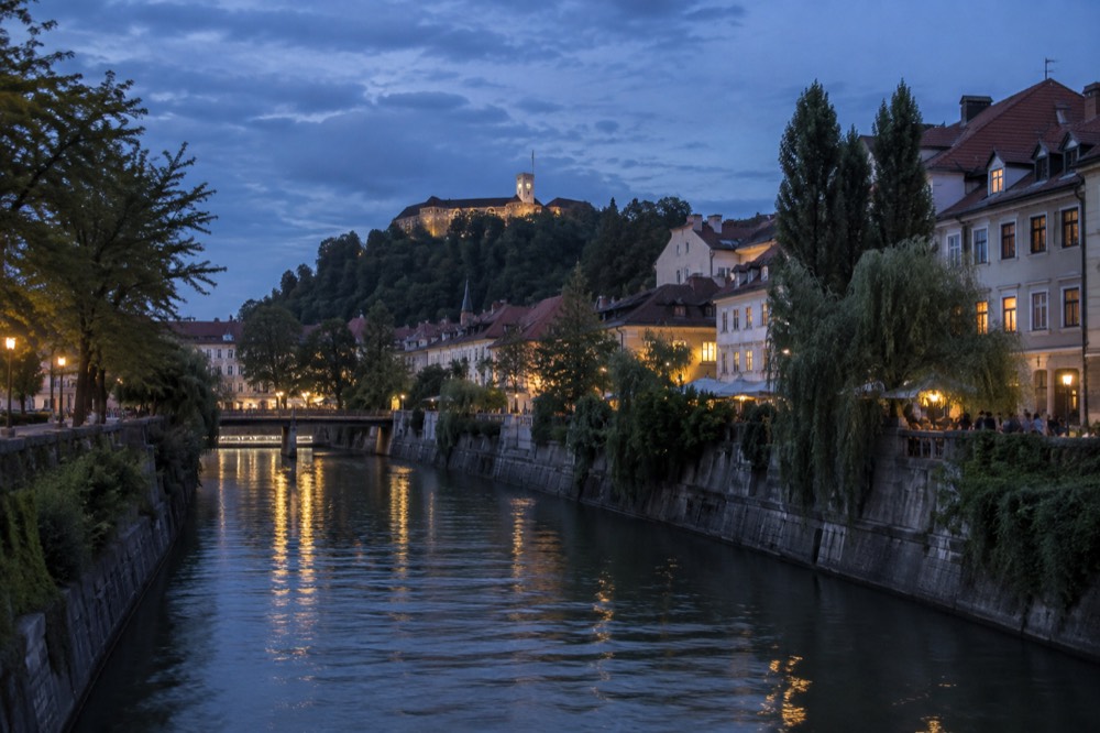 View across the Ljubljanica river towards Ljubljana Castle on its wooded hill at dusk