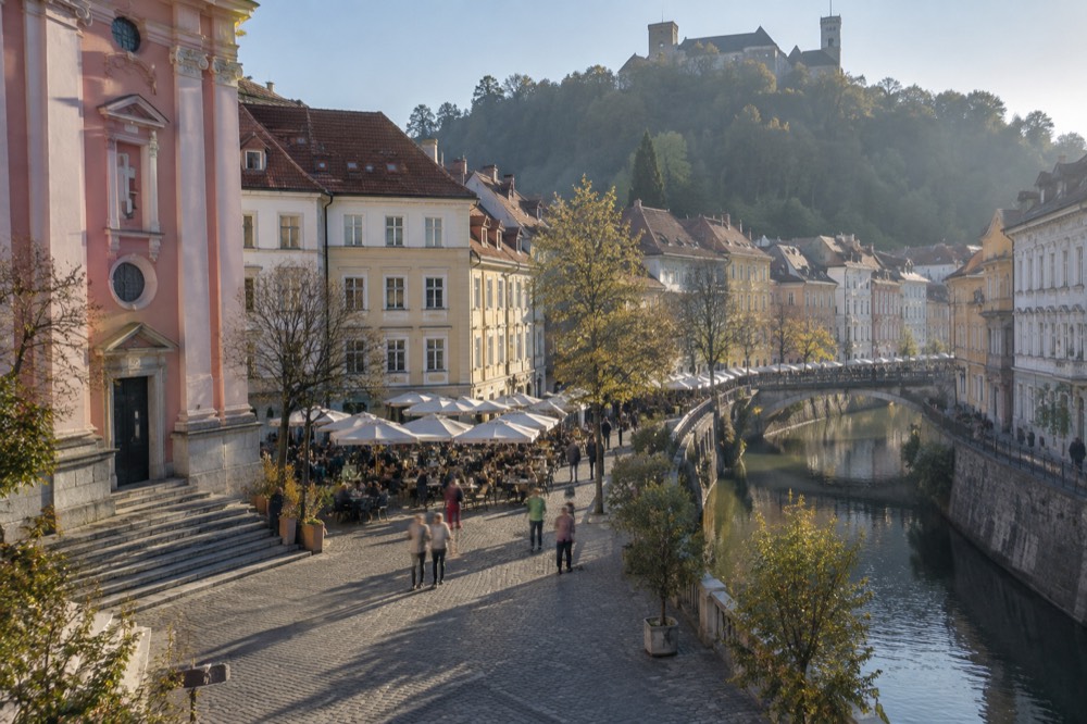 A pedestrian square with café tables in front of a pink church facade
